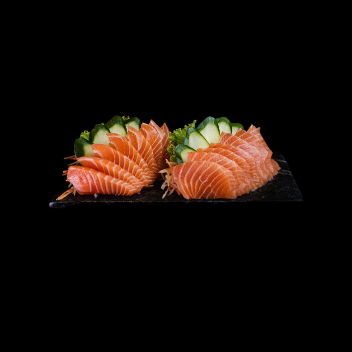 Delicious salmon sashimi beautifully arranged with cucumber on slate plate.