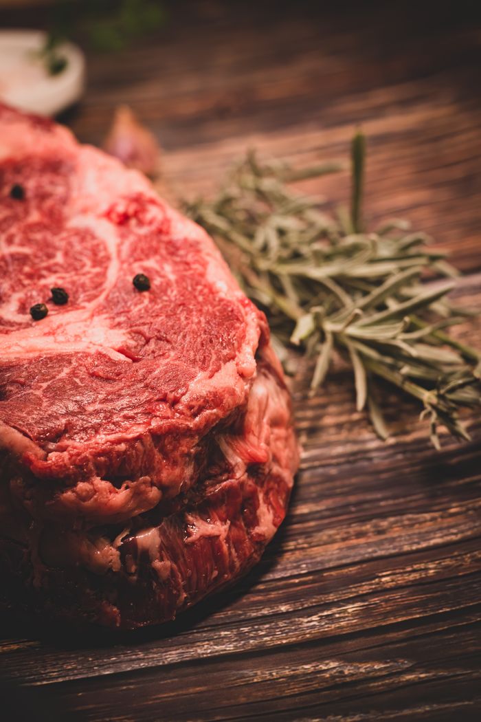 Close-up of a raw beef steak seasoned with rosemary and peppercorns on a wooden surface.